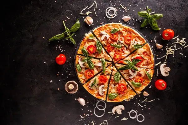 Krojona pizza z pomidorami, pieczarkami i bazylią na czarnym tle, otoczona składnikami.